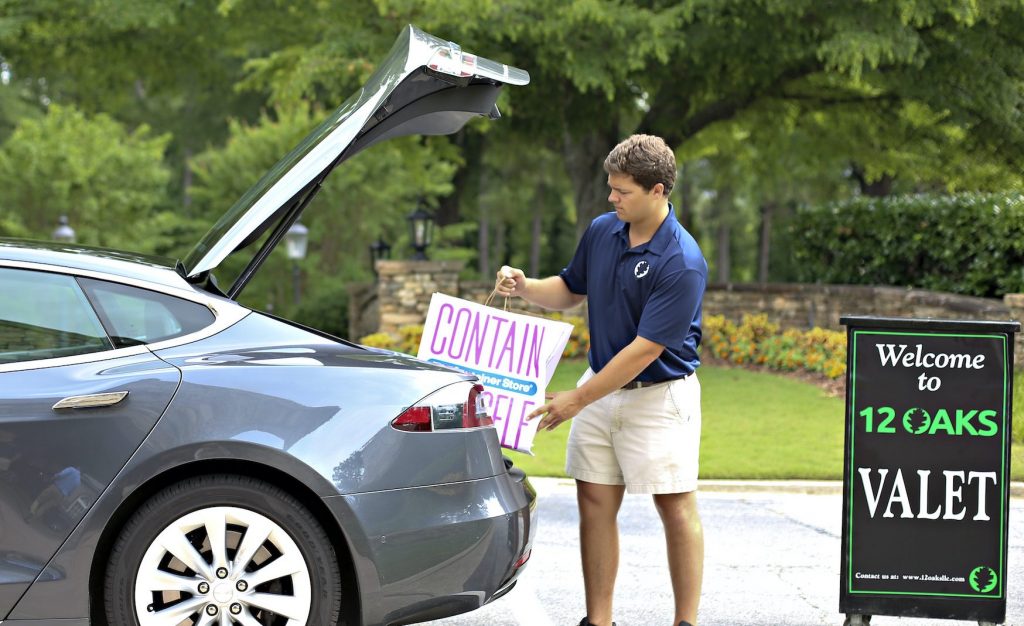 Valet attendant placing a reserved parking sign in the trunk of a car at a 12 Oaks valet service location.