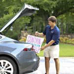 Valet attendant placing a reserved parking sign in the trunk of a car at a 12 Oaks valet service location.