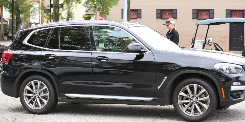 Valet attendant walking alongside a parked SUV near a valet stand and golf cart in a service area.