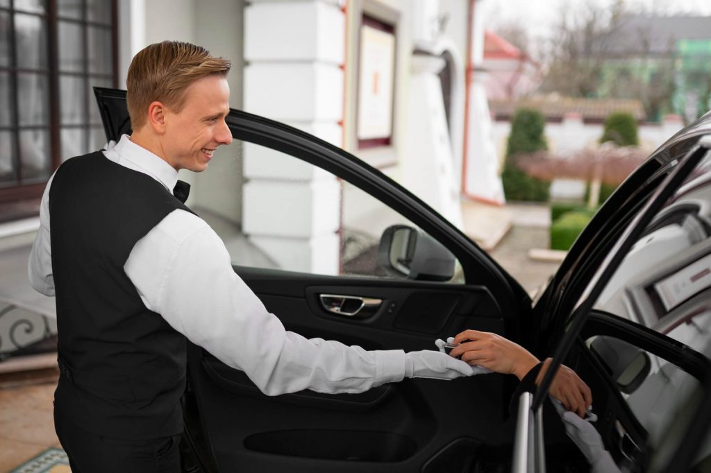 Valet attendant in uniform handing car keys to a driver at a hotel entrance, providing parking service.
