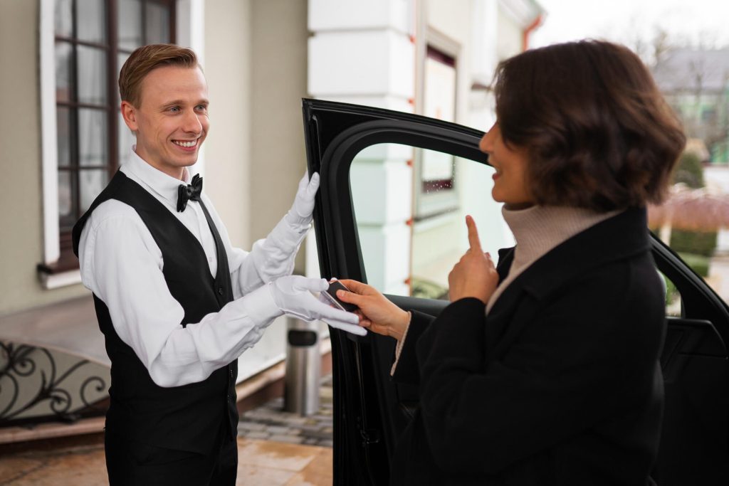 Valet attendant in formal uniform handing car keys to a guest at a building entrance.