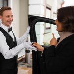 Valet attendant in formal uniform handing car keys to a guest at a building entrance.