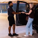 Valet attendant receiving a ticket from a customer at a covered parking garage entrance outside a restaurant.