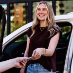 Customer handing valet ticket to an attendant while standing beside an open car door.