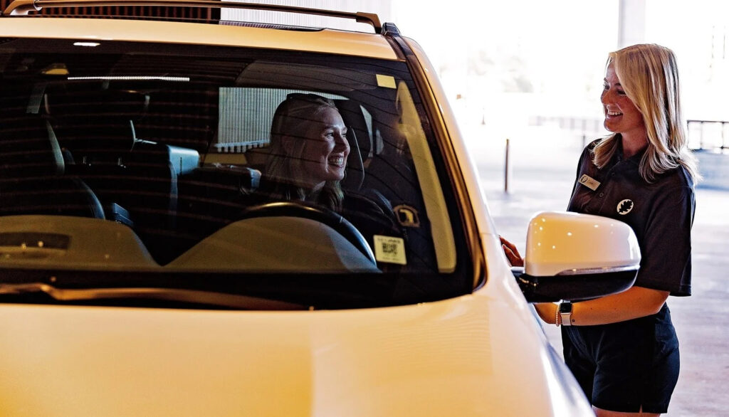 Valet attendant greeting a driver at a covered parking entrance while assisting with vehicle drop-off.