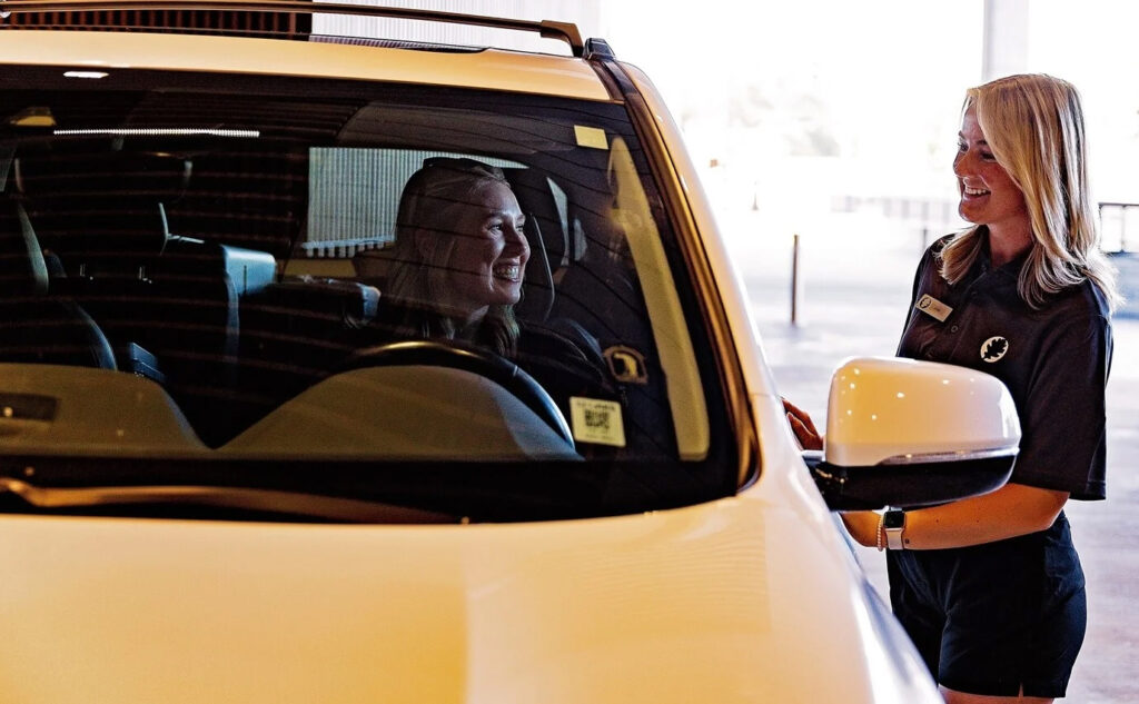 Valet attendant greeting a driver at a covered parking entrance while assisting with vehicle drop-off.
