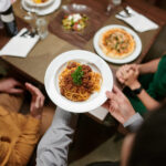 Server delivering a freshly prepared pasta dish to guests dining at an upscale restaurant.